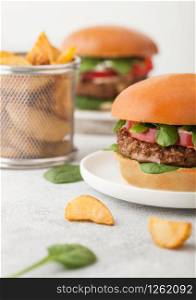 Healthy vegetarian meat free burgers on round chopping board with vegetables on light background with potato wedges.