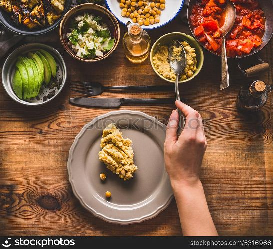 Healthy vegetarian salad bar. Women female hand with spoon puts food on a plate, top view. Clean eating or diet food concept