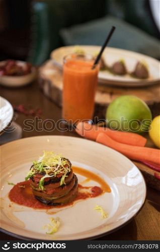 Healthy vegeterian food on brown wood board. Baked vegetables in layers, fruits and carrot juice. Baked vegetables in layers, fruits and carrot juice