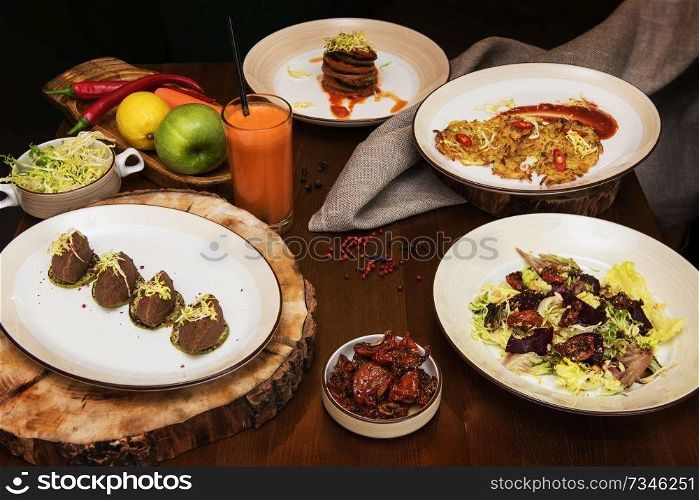 Healthy vegeterian food on brown wood board. Spring vitamin dieting food. Salad from beet with dried tomatoes and cabbage, potato vegan pancakes, dried tomatoes, pate from red beans, baked vegetables in layers, fruits and carrot juice. Healthy vegeterian food