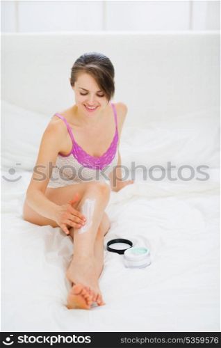 Healthy woman applying creme on leg in bed