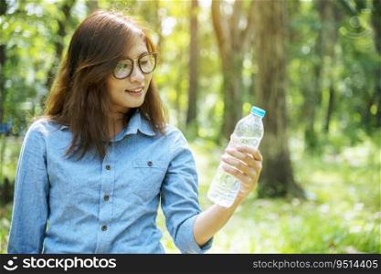 Healthy woman holding mineral drinking water in hands outdoor outside town in green park smile and looking at camera with happy face. Young woman happy outdoor lifestyle holding water bottle.
