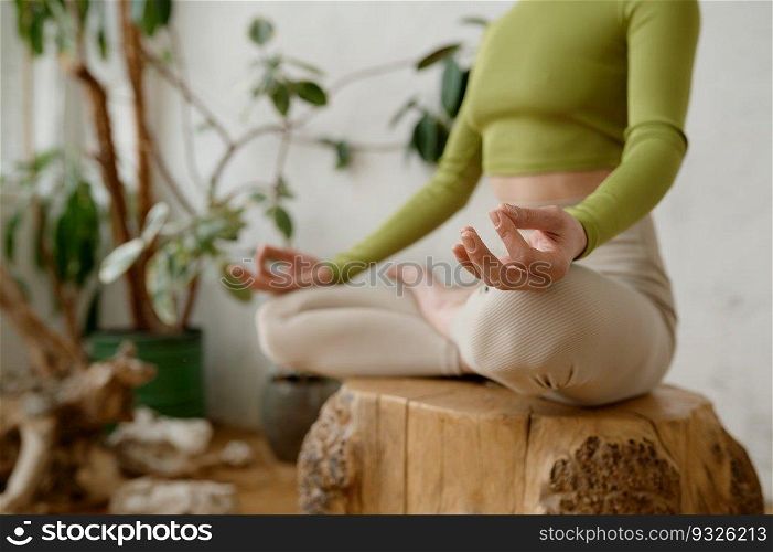 Healthy woman practicing meditation and relaxation yoga exercise indoors. Sportswoman doing Ardha Padmasana with mudra gesture for chakra harmony achievement. Crop shot. Healthy woman practicing meditation and relaxation yoga exercise indoors