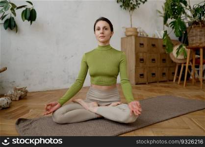 Healthy woman practicing meditation and relaxation yoga exercise indoors. Sportswoman doing Ardha Padmasana with mudra gesture for chakra harmony achievement. Healthy woman practicing meditation and relaxation yoga exercise indoors