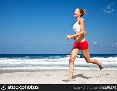 Healthy woman running on the beach, doing sport outdoor, freedom, vacation, heath care concept with copy space over natural blue background