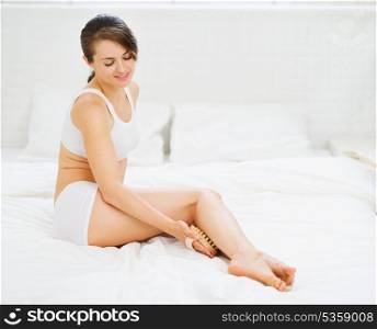 Healthy woman sitting on bed and massaging her legs