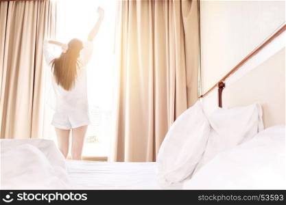 Healthy Woman stretching in bed room and open the curtains after wake up, back view, lifestyle people in cozy indoor comfortable relaxing space.