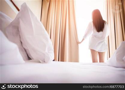 Healthy Woman stretching in bed room and open the curtains after wake up, back view, lifestyle people in cozy indoor comfortable relaxing space.