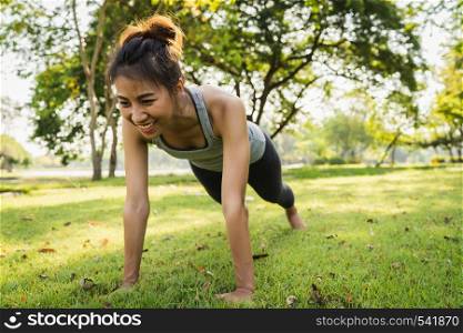 Healthy young Asian runner woman warm up her body by push up before exercise and yoga near lake at park under warm light morning. Lifestyle fitness and active women exercise in urban city concept.