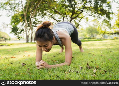 Healthy young Asian runner woman warm up her body by push up before exercise and yoga near lake at park under warm light morning. Lifestyle fitness and active women exercise in urban city concept.