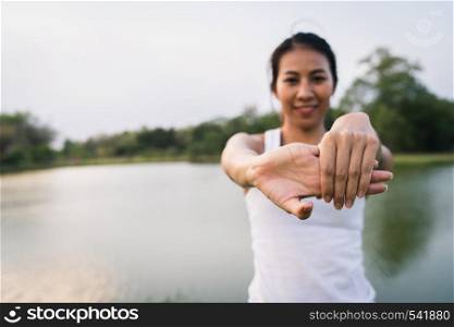 Healthy young Asian runner woman warm up the body stretching before exercise and yoga near lake at park under warm light morning. Lifestyle fitness and active women exercise in urban city concept.
