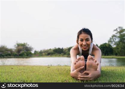 Healthy young Asian runner woman warm up the body stretching before exercise and yoga near lake at park under warm light morning. Lifestyle fitness and active women exercise in urban city concept.