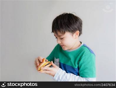 Healthy young boy eating burger. A child holding cheeseburger and looking with smiling face, Isolated Happy Kid having fast food hamburger for snack. Favorite children"s food.