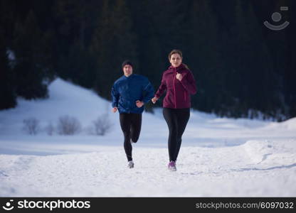 healthy young couple jogging outside on snow in forest. athlete running on beautiful sunny winter day