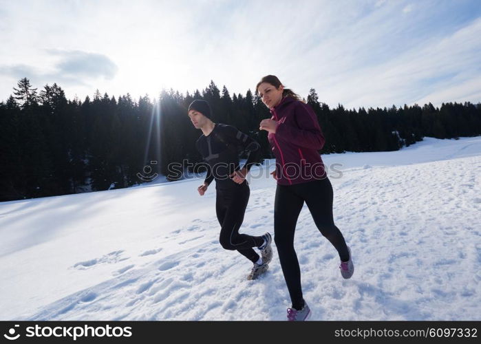 healthy young couple jogging outside on snow in forest. athlete running on beautiful sunny winter day