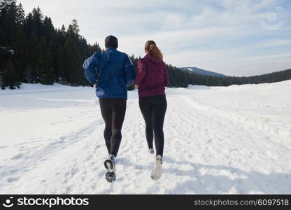 healthy young couple jogging outside on snow in forest. athlete running on beautiful sunny winter day