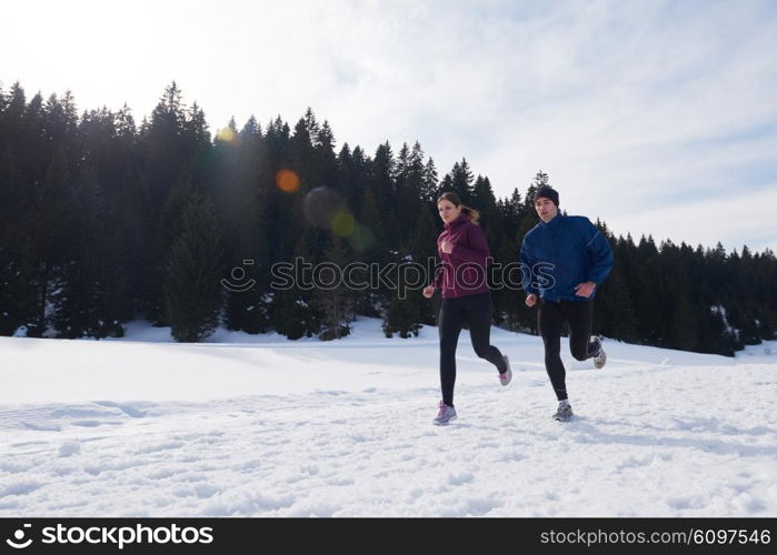 healthy young couple jogging outside on snow in forest. athlete running on beautiful sunny winter day