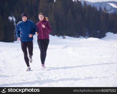 healthy young couple jogging outside on snow in forest. athlete running on beautiful sunny winter day