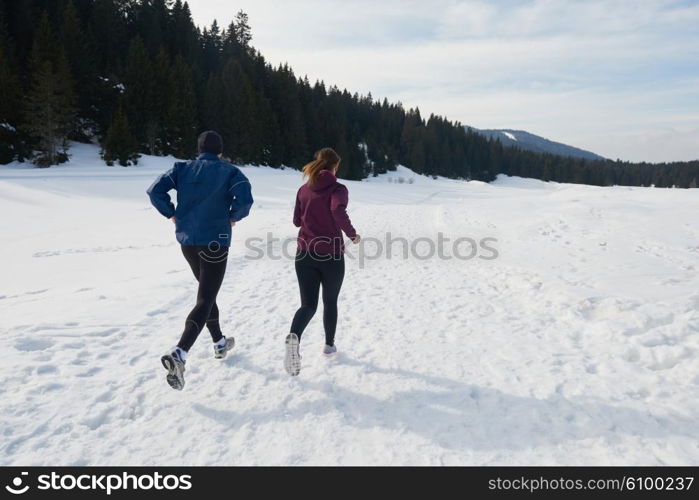 healthy young couple jogging outside on snow in forest. athlete running on beautiful sunny winter day