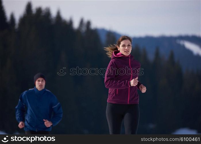 healthy young couple jogging outside on snow in forest. athlete running on beautiful sunny winter day