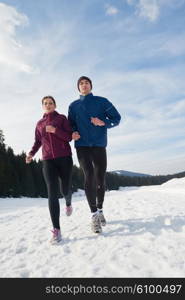 healthy young couple jogging outside on snow in forest. athlete running on beautiful sunny winter day