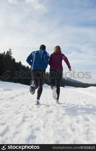 healthy young couple jogging outside on snow in forest. athlete running on beautiful sunny winter day