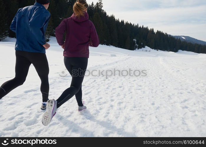 healthy young couple jogging outside on snow in forest. athlete running on beautiful sunny winter day