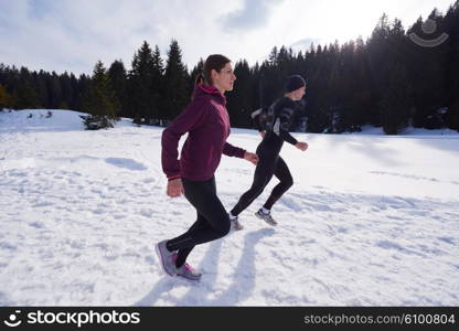 healthy young couple jogging outside on snow in forest. athlete running on beautiful sunny winter day