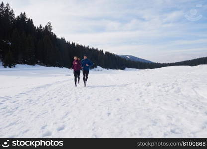 healthy young couple jogging outside on snow in forest. athlete running on beautiful sunny winter day