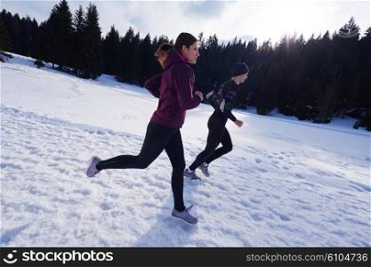 healthy young couple jogging outside on snow in forest. athlete running on beautiful sunny winter day