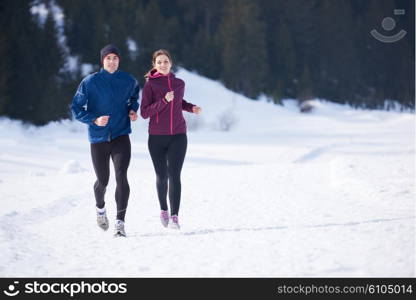 healthy young couple jogging outside on snow in forest. athlete running on beautiful sunny winter day