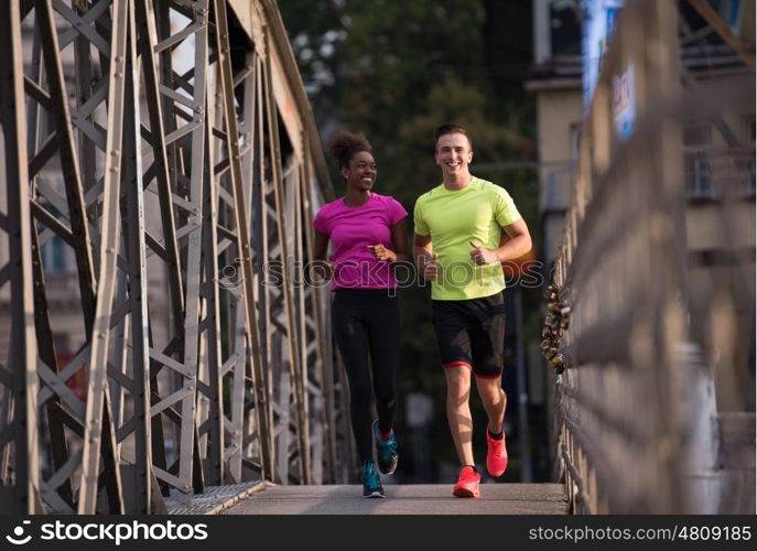 healthy young multiethnic couple jogging across the bridge in the city at early morning with sunrise in background