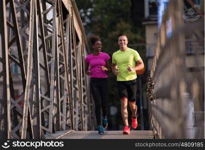 healthy young multiethnic couple jogging across the bridge in the city at early morning with sunrise in background