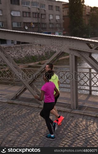 healthy young multiethnic couple jogging in the city at early morning with sunrise in background