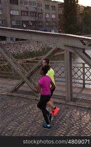 healthy young multiethnic couple jogging in the city at early morning with sunrise in background