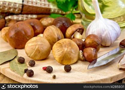 Heap butter mushrooms with garlic, spices, bay leaf, knife, decanter with vegetable oil, wipe on the background of wooden boards
