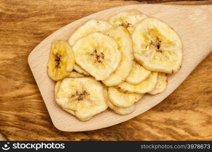 Heap of banana chips, dehydrated slices on wooden spoon. Heap of dried banana chips on wooden spoon