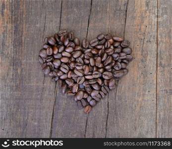 heap of beans of coffee formng a heart on a rustic wooden background