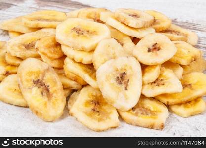Heap of dried organic banana chips on rustic board. Dried organic banana chips on rustic board
