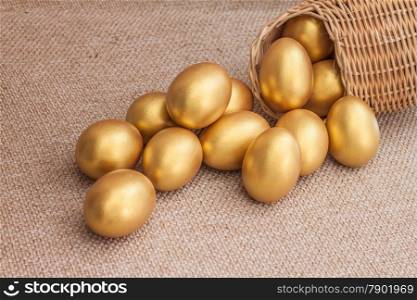 Heap of golden easter egg in wicker basket on brown sack background
