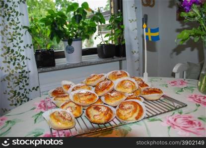 Heap of newly baked delicious cinnamon buns at a kitchen table, decorated with a swedish flag
