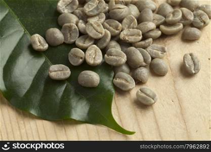 Heap of Pamwamba green unroasted coffee beans and a coffee plant leaf