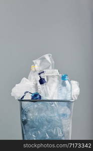 Heap of plastic bottles, cups, bags collected to recycling in a metal bin. Concept of plastic pollution and too many plastic waste. Trash with used plastic packagings over grey background with copy space at the top