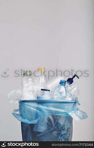 Heap of plastic bottles, cups, bags collected to recycling in a metal bin. Concept of plastic pollution and too many plastic waste. Trash with used plastic packagings over grey background with copy space at the top