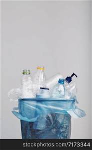 Heap of plastic bottles, cups, bags collected to recycling in a metal bin. Concept of plastic pollution and too many plastic waste. Trash with used plastic packagings over grey background with copy space at the top