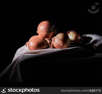 heap of unpeeled round brown onions on a gray linen napkin, black background