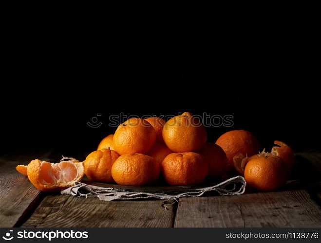 heap of unpeeled round ripe orange mandarin on a gray linen napkin, wooden table, low key