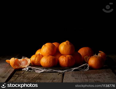 heap of unpeeled round ripe orange mandarin on a gray linen napkin, wooden table, low key