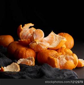 heap of unpeeled round ripe orange mandarin on a gray linen napkin, wooden table, low key
