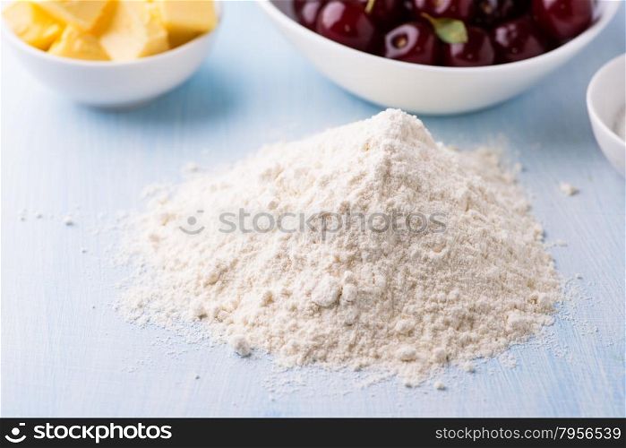 Heap of wheat flour on table, cherry and butter on side, selective focus. Baking ingredients.